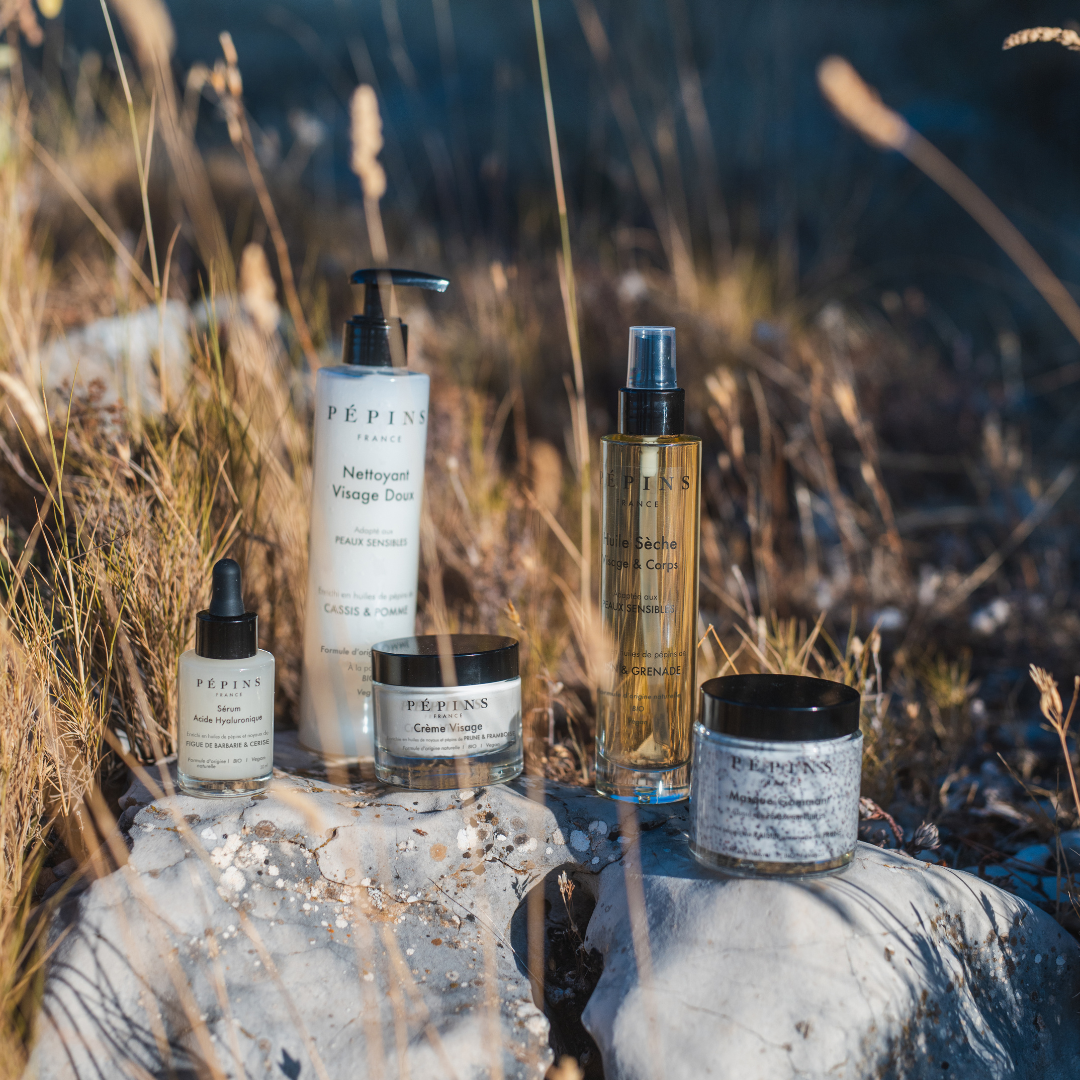 Les soins ROUTINE 8 PÉPINS présentés en extérieur parmi des éléments naturels, illustrant un rituel de beauté clean.